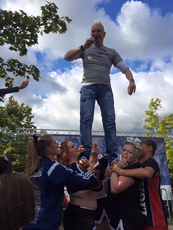 Sunny mit Mikrofon, bei einer Veranstaltung von einer Sportgruppe hochgehoben